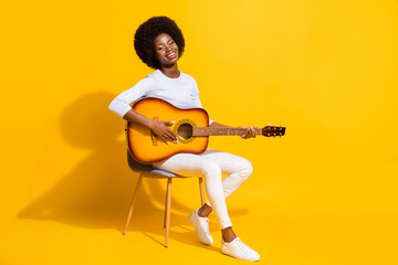 Full length profile portrait of adorable cheerful dark skin girl playing guitar isolated on yellow color background © deagreez
