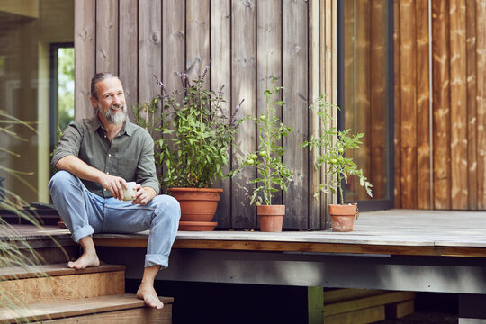 Smiling bearded man holding coffee cup while sitting outside tiny house