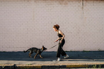 Woman training dog at sidewalk against wall