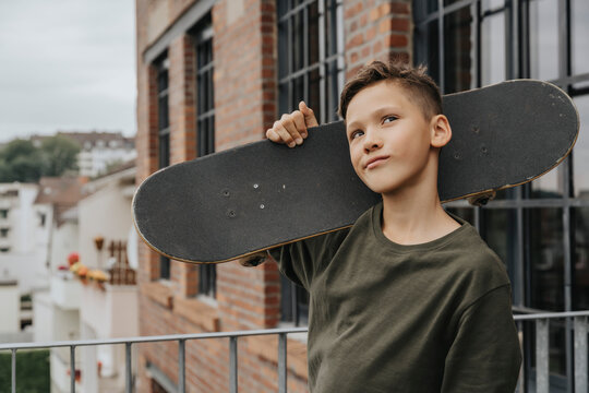 Thoughtful boy posing with skateboard while standing against building