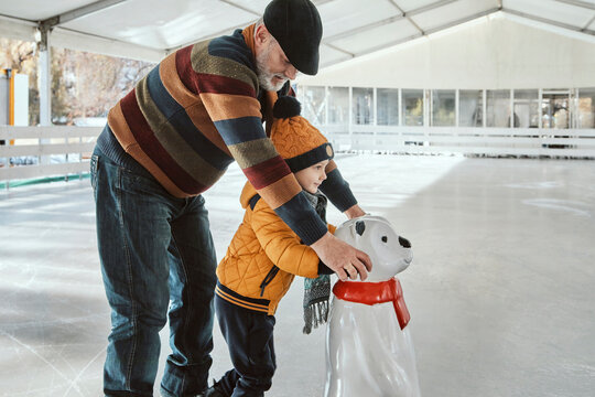 Grandfather and grandson on the ice rink, ice skating, using ice bear figure as prop