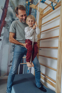 Happy father assisting son climbing rope in living room