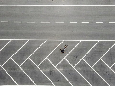 Drone view of man lying on back in empty parking lot