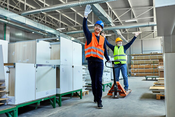 Two workers with pallet jack having fun in factory