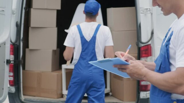 Two young workers of removal company are loading boxes and furniture into a minibus