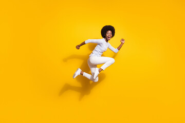 Fototapeta na wymiar Full body profile side photo of afro american young woman jump up run wear white pullover pants isolated on yellow color background