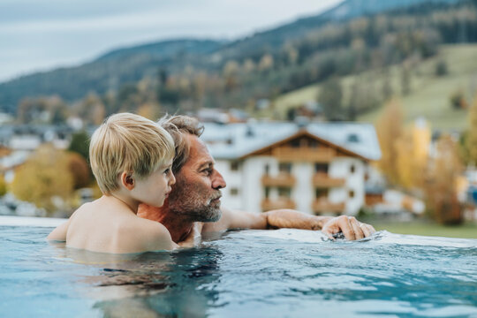 Father and son in infinity pool looking away at Salzburger Land, Austria