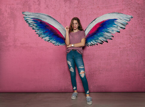 Teenage girl standing against angel wings graffiti on pink wall