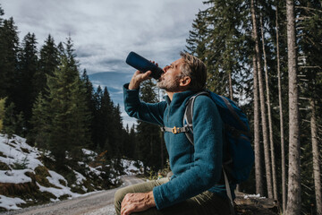 Male tourist drinking water while sitting against trees at Salzburger Land, Austria