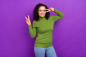 Photo of funny adorable afro woman wear green turtleneck showing v-sign cover eye smiling isolated purple color background