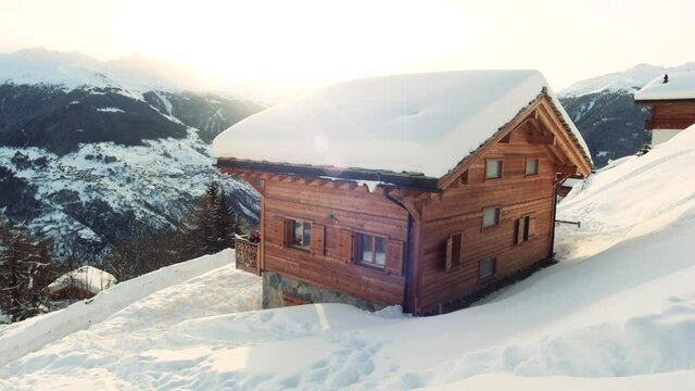 Traditional wooden chalet with epic view over the snowy mountains. Snow in wintertime in the Alps. 2 kids on the balcony waving towards the camera. Sunset in background.