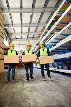 Three workers carrying boxes in factory warehouse