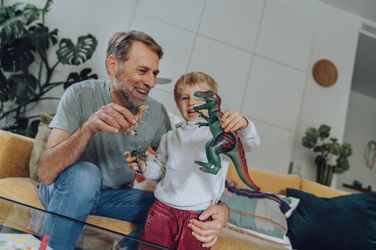Father and son playing with dinosaur toy in living room