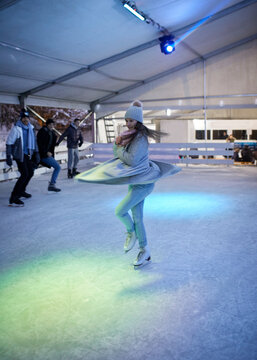 Young woman doing a pirouette on an ice rink at night watched by her friends
