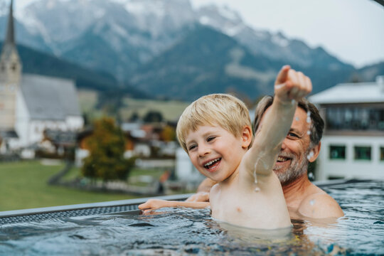 Happy father and son enjoying in infinity pool with town in background at Salzburger Land, Austria