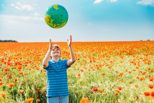 Happy boy catching globe while standing in poppy field against sky on sunny day
