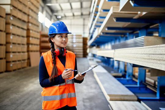 Smiling female worker with clipboard in factory warehouse