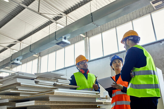Two men and woman in reflective vests discussing in factory