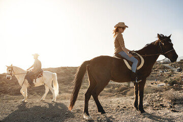 Young couple riding horses doing excursion at countryside during sunset time - Focus on woman