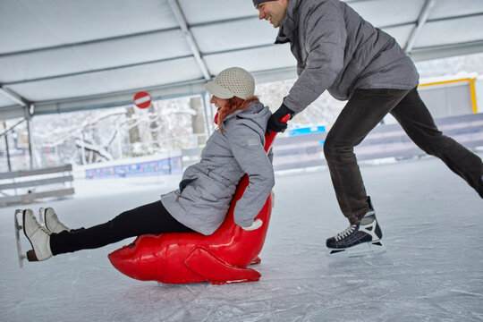 Couple ice skating, using seal sledge to push woman