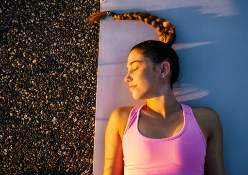 Young woman with eyes closed meditating while lying on mat at sunset
