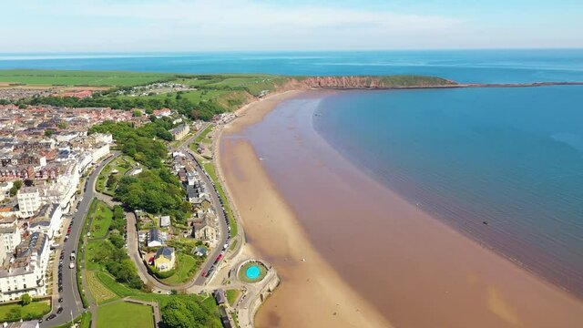 Aerial footage of the beach front in the town of Filey in the UK showing people relaxing and having fun on the beach on a sunny summers day