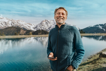 Happy mature man holding mobile phone while standing against Prinzensee, Salzburger Land, Austria