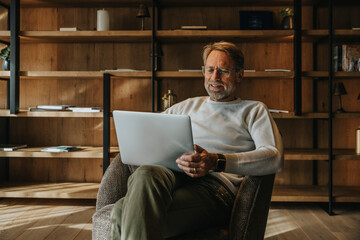 Mature man using laptop while sitting on armchair
