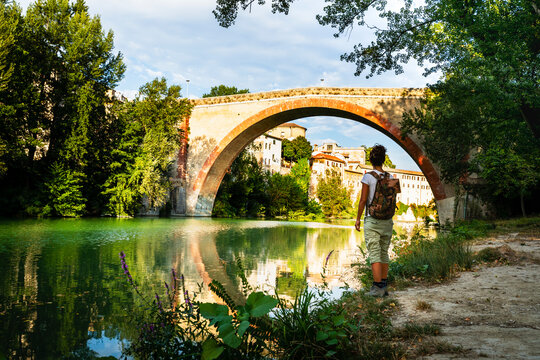 Woman standing and looking at ancient Ponte Della Concordia bridge at Fossombrone, Marche, Italy