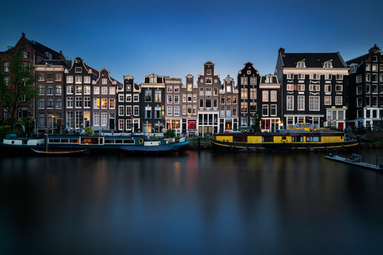 Netherlands, Amsterdam, Various boats moored along city canal with row of houses in background