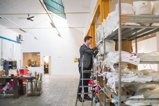Businessman standing on step ladder at shelf in a warehouse