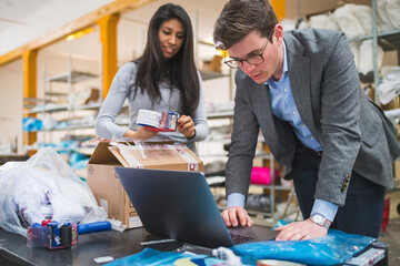 Businessman using laptop and female employee packing merchandise in a warehouse