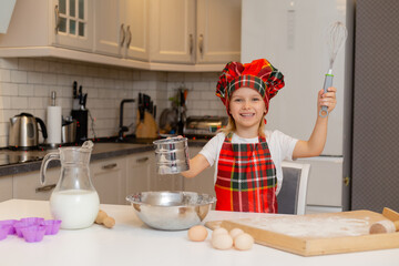 little happy smiling blonde girl in a chef costume kneads dough for Christmas baking in the...