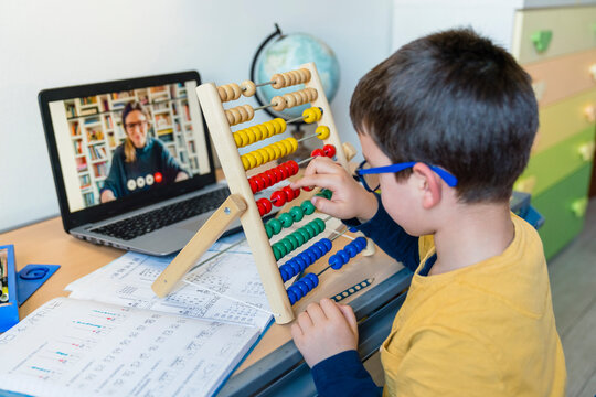 Male student with abacus at desk while teacher on video call during COVID-19 homeschooling