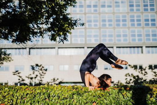 Young woman performing yoga on grass in city park during sunny day