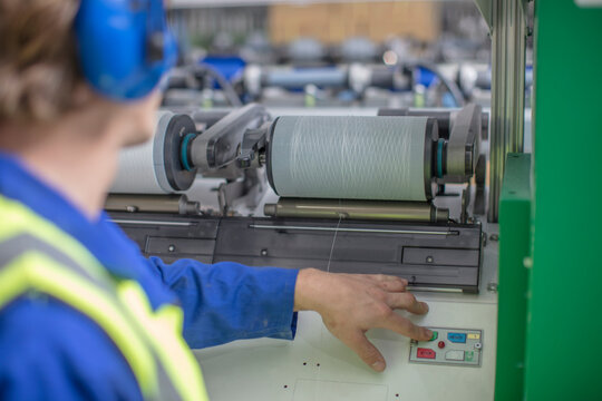 Man wearing ear defenders operating spool machine in factory