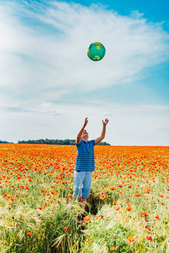 Boy catching globe while standing in poppy field against sky