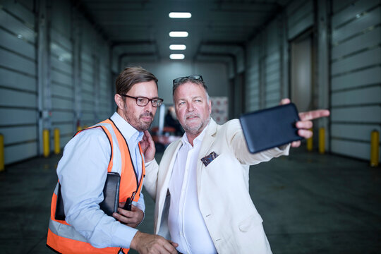 Man in reflective and businessman with cell phone talking in industrial hall