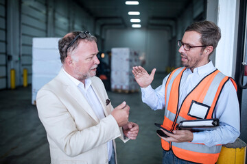 Businessman and man in reflective vest talking in industrial hall