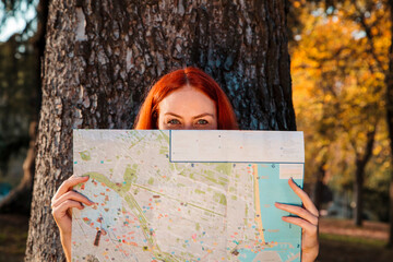 Mid adult woman holding map in front of face against tree in park