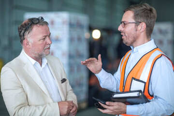 Businessman and man in reflective vest talking in industrial hall