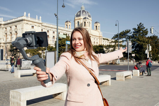 Austria, Vienna, portrait of smiling young woman using selfie-stick for taking photo with smartphone