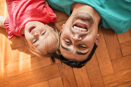 Portrait of father and little daughter lying on the floor at home having fun