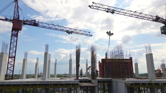 Tower cranes and workers at high concrete residential building under construction. Real estate development concept.