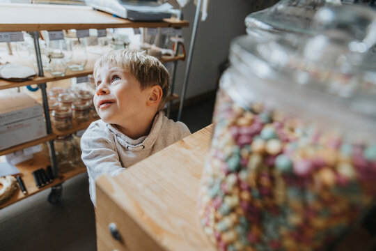 Blond little boy day dreaming while standing in candy store