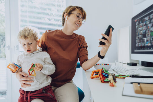 Mother using smart phone while son sitting on her lap playing with toys