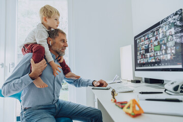 Father carrying son on shoulder while attending video conference at home office