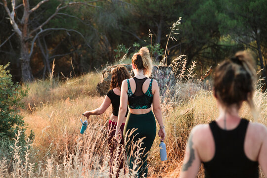 Female friends in sports clothing walking on trail in field during vacation