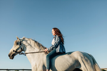 Young woman on horse at equestrian center against clear sky