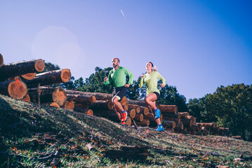 Mature couple running on land against clear blue sky in forest